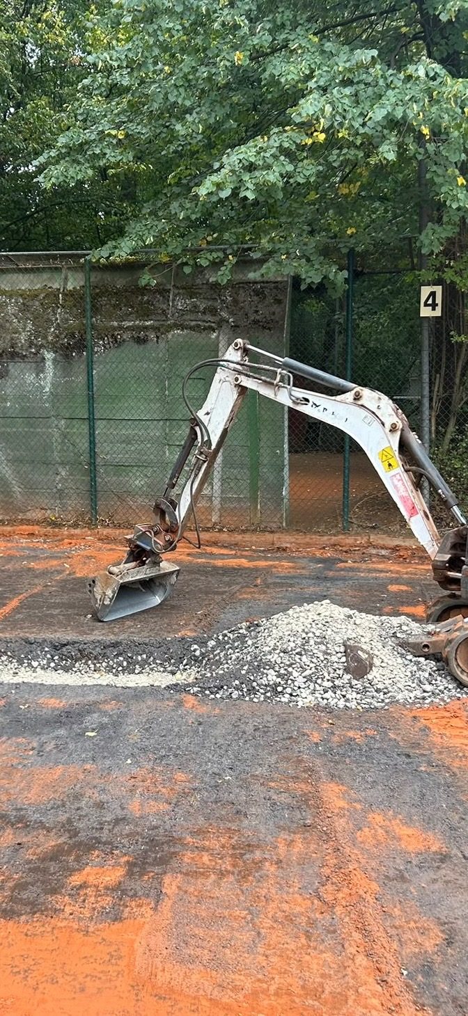 Minibagger auf der abgetragenen Fläche neben Platz 4, davor ein Haufen Kies