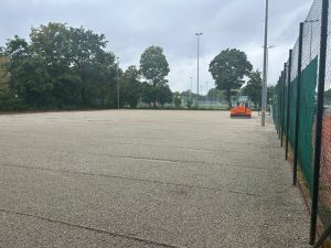 Eben abgezogene Feinkiesfläche auf den hinteren Plätzen 4 bis 6, rechts am Zaun eine orange Baumaschine