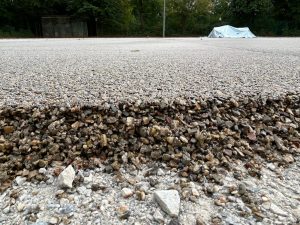 Flacher Blick über einen der hinteren Plätze: vorne die offene Kante aus grobem Kies und Schotter, dahinter die frisch verklebte helle Schicht bis zum Zaun