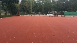 Fertig verlegte HarTru TopSand Membran auf einem der hinteren Plätze, im Hintergrund die Baustelle mit Minibagger und abgedecktem Material