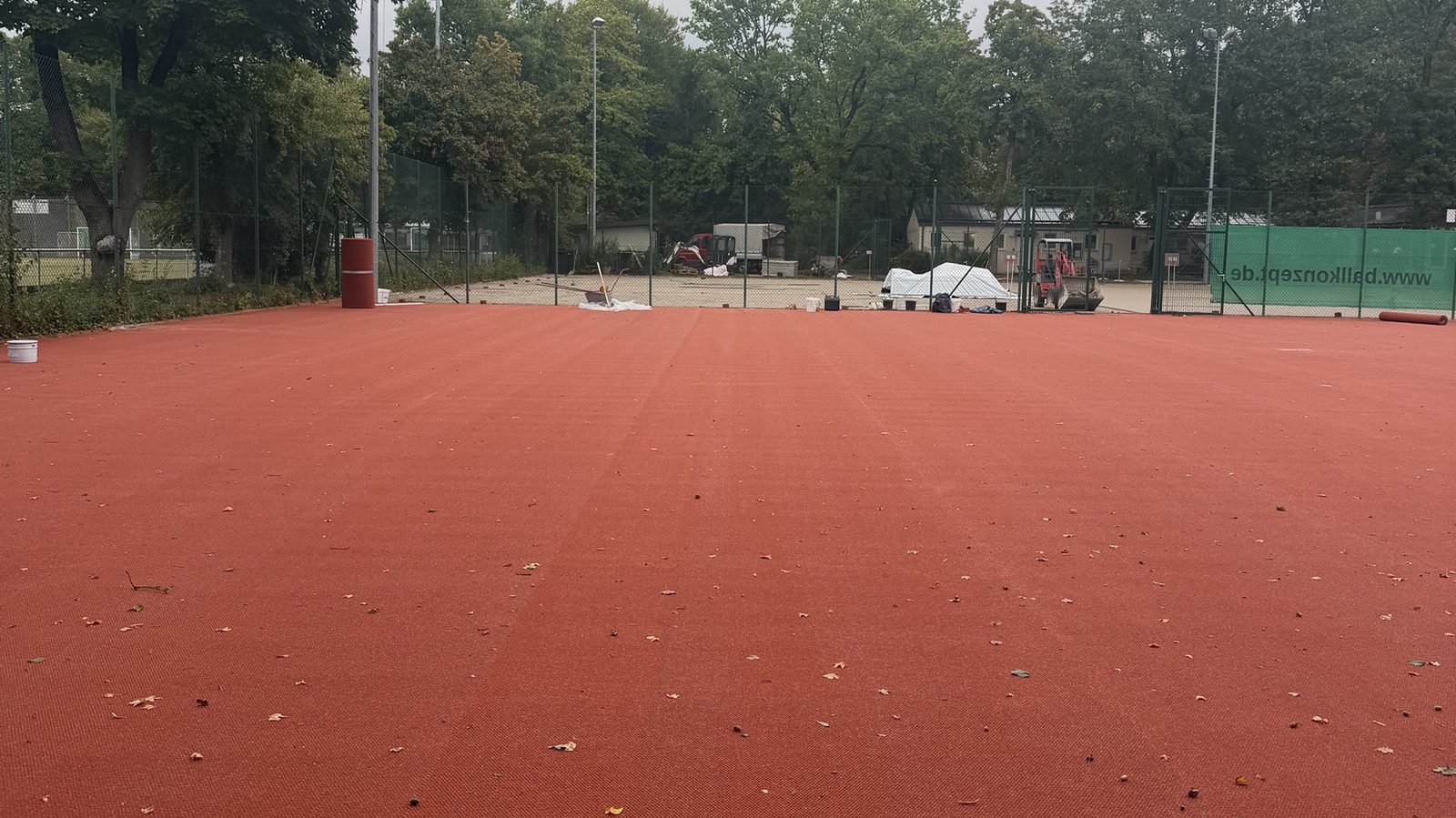 Fertig verlegte HarTru TopSand Membran auf einem der hinteren Plätze, im Hintergrund die Baustelle mit Minibagger und abgedecktem Material